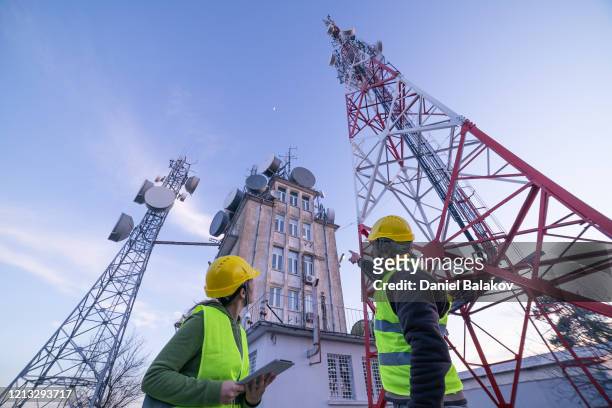 電気通信タワーの近くのフィールドで働くエンジニア。チームワーク。 - アンテナ ストックフォトと画像