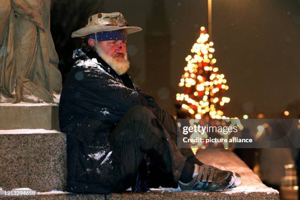 Trotz Kälte und Schnee sitzt der wohnungslose Franz-Georg Rauschmann am an einer Straße in Lübeck - im Hintergrund leuchtet ein Weihnachtsbaum. Der...