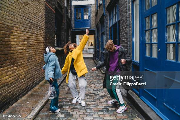 drei glückliche freunde tanzen zusammen in der stadt - london fashion stock-fotos und bilder
