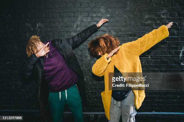 deux jeunes adultes faisant le mouvement de tamponnage contre un mur noir de briques - dab photos et images de collection