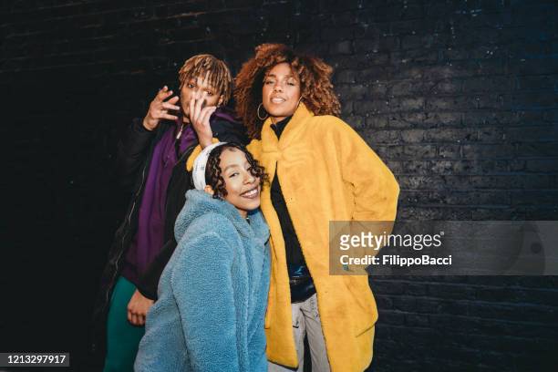 drei freunde tanzen in der stadt gegen eine schwarze backsteinmauer - rap stock-fotos und bilder