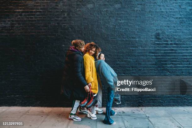 three friends dancing in the city against a black brick wall - moda da rua imagens e fotografias de stock