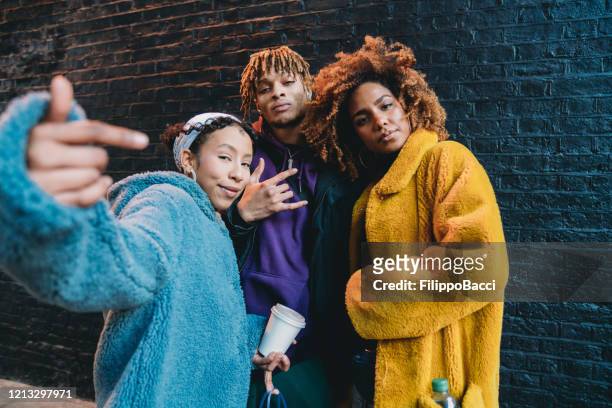 portrait of three friends against a black bricks wall, making gestures in front of the camera - cool attitude stock pictures, royalty-free photos & images