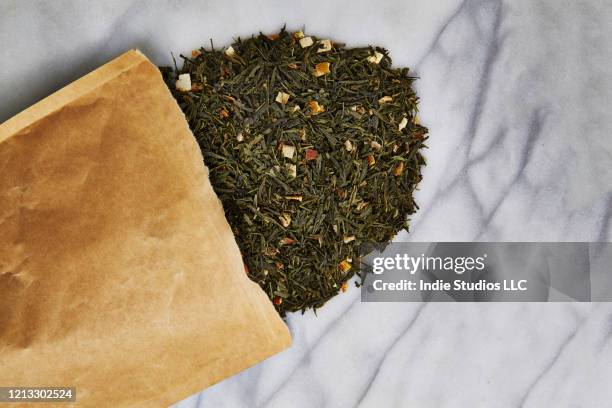 directly above photo of loose tea spilling out of brown paper bag over marble stone background - green tea leaves stock pictures, royalty-free photos & images