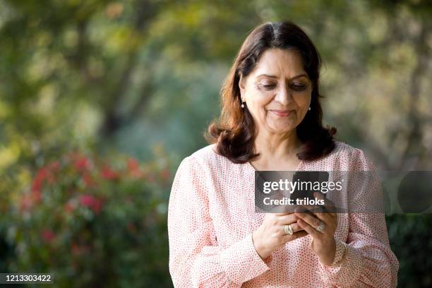 senior woman using mobile phone at park - india woman stock pictures, royalty-free photos & images