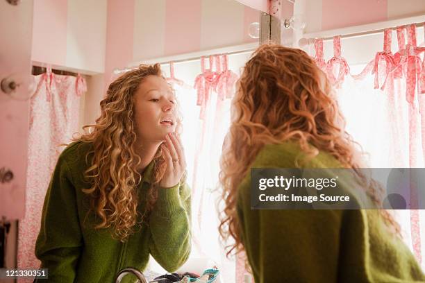 teenage girl checking skin in bathroom mirror - pimple stockfoto's en -beelden