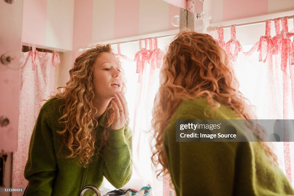 Teenage girl checking skin in bathroom mirror