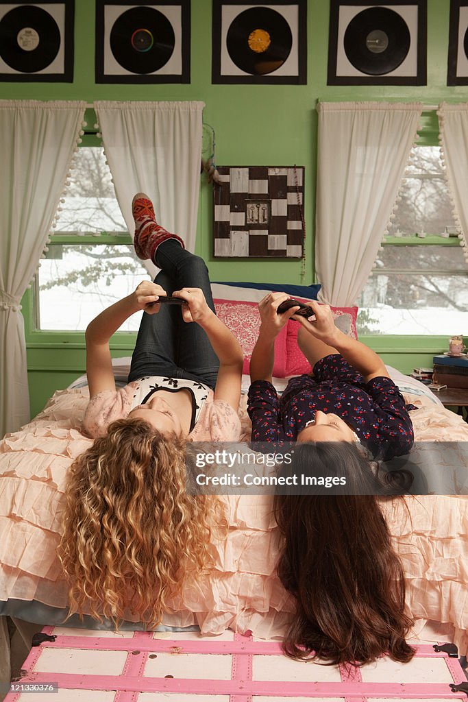 Teenage girls lying on bed with smartphones