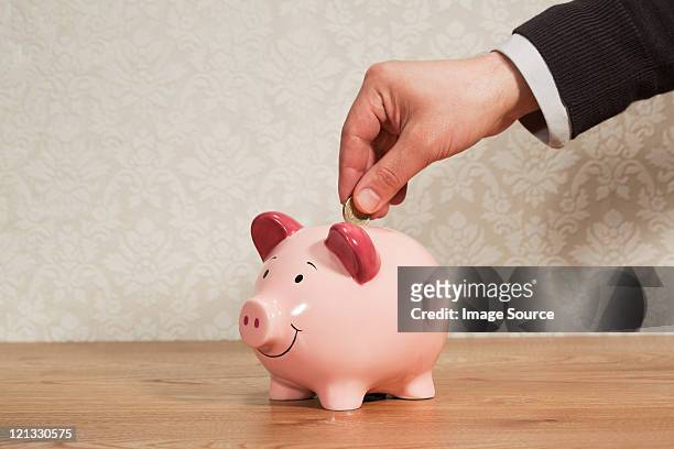 man inserting pound coin into piggy bank - inserting stock pictures, royalty-free photos & images