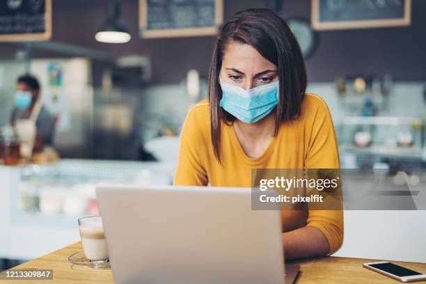 femme inquiété avec un masque de visage regardant un ordinateur portatif - medical news photos et images de collection