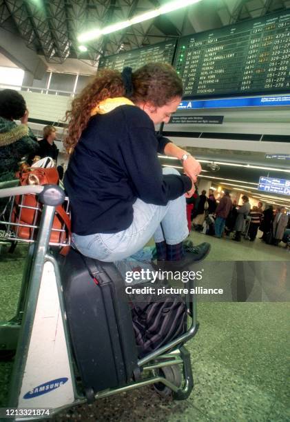 Eine junge Frau sitzt am 5.1.1997 in der Abfertigungshalle des Frankfurter Flughafens auf ihrem Gepäckwagen und schaut auf die Uhr. Neuerliche...