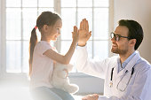 Happy little preschool girl giving high five to male doctor.