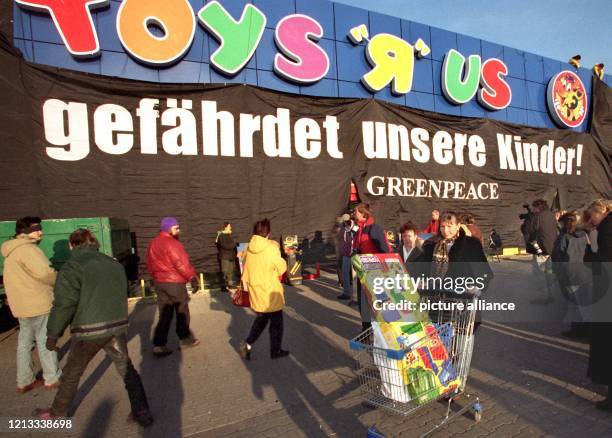 Mit einem gefüllten Einkaufswagen geht eine Frau am aus einem Spielzeugmarkt, dessen Fassade von Greenpeace mit einem Transparent verhängt wurde. Die...