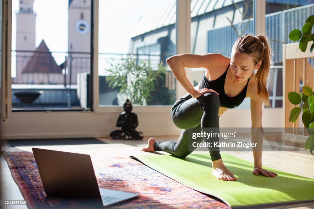 Woman exercising at home in front of her laptop, stretching her legs