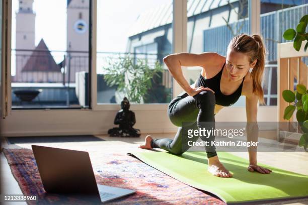 woman exercising at home in front of her laptop, stretching her legs - fitness fotografías e imágenes de stock