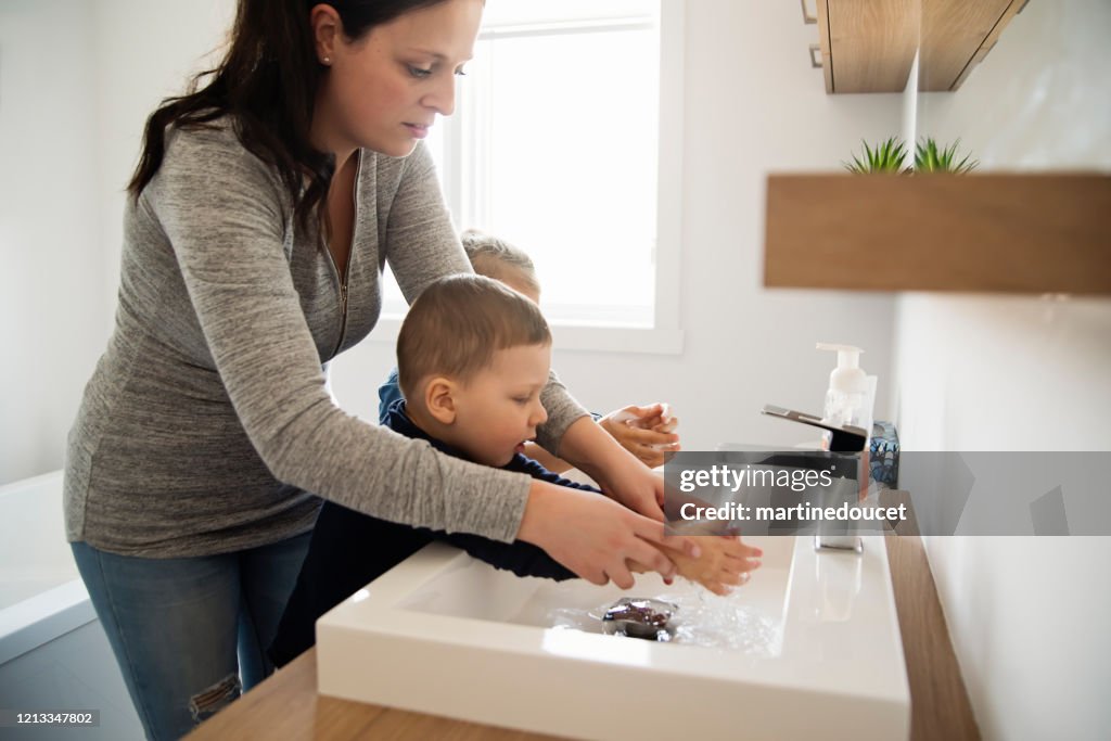 Mãe ensinando crianças pequenas como lavar as mãos em isolamento de quarentena Covid-19