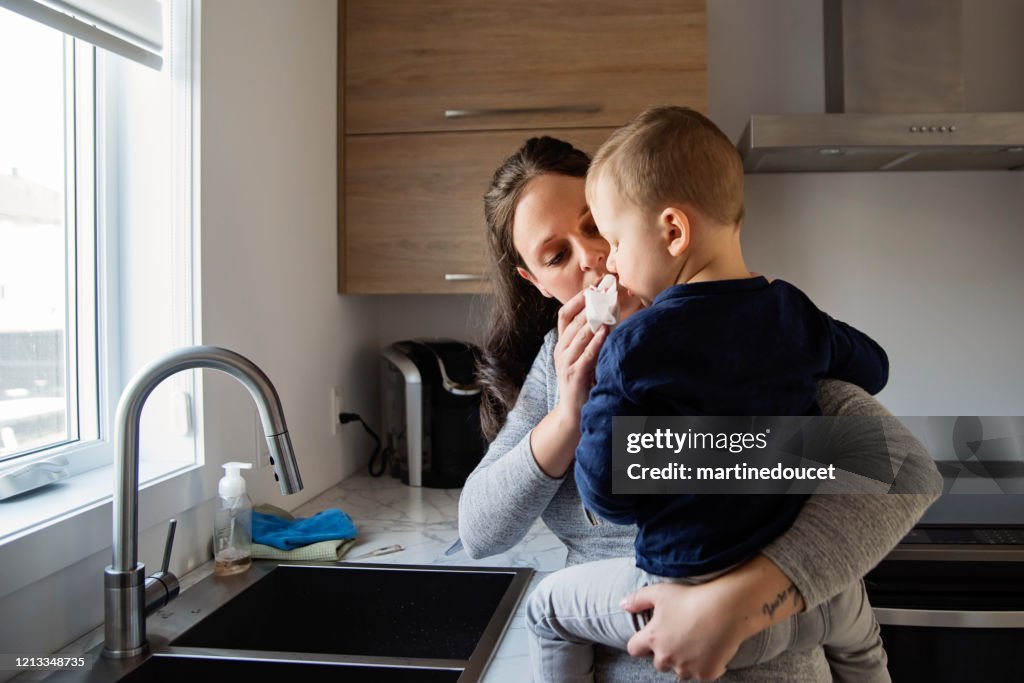 Millennial woman wiping son's nose while in quarantine isolation Covid-19