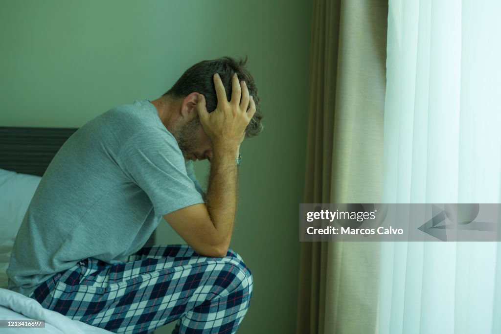 Dramatic portrait of attractive scared and depressed 40s man on bed in pajamas feeling worried suffering anxiety and depression problem during virus quarantine home lockdown