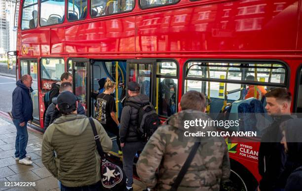 Commuters, some wearing PPE , including a face mask as a precautionary measure against COVID-19, wait to board a TFL red London bus at Vauxhall bus...