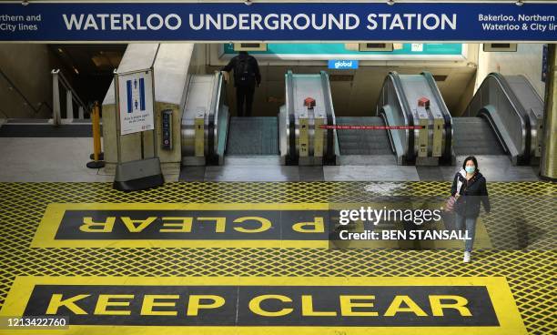 Commuter, wearing PPE , including a face mask as a precautionary measure against COVID-19, walks over a new "Keep Clear" floor sign, to help...