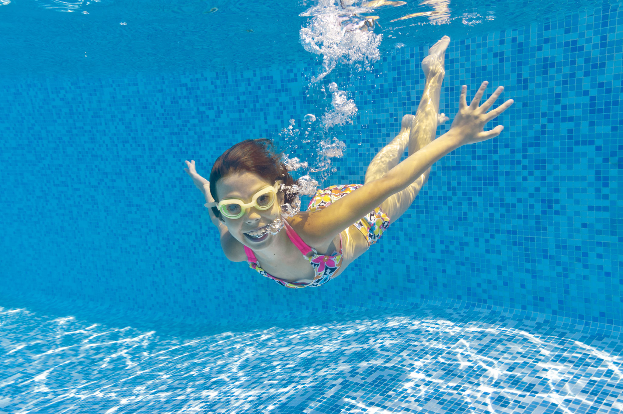 A smiling child swimming underwater in a pool in goggles A smiling child swimming underwater in a pool in goggles