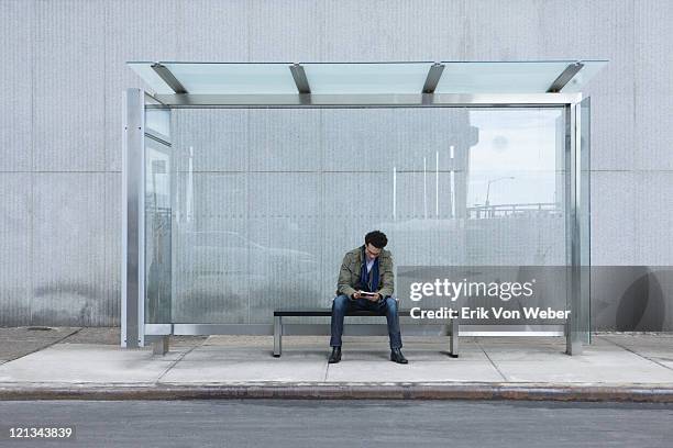 man sitting at glass bus stop with handheld device - sitting at desk stock pictures, royalty-free photos & images