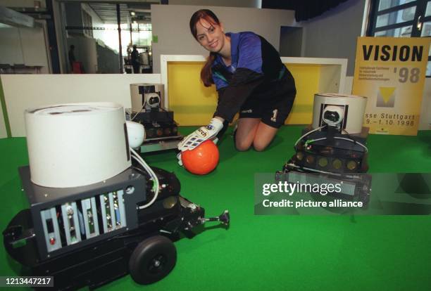 Die Aufnahme vom 28.9.1998 zeigt drei fußballspielende Roboter und eine Hostess als Torhüterin bei einer Pressevorstellung auf der Messe VISION '98...