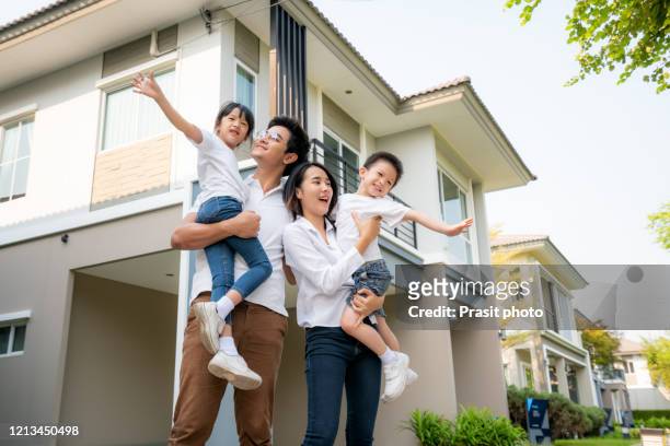 asian family with father and mother standing and carry daughter and son in front of their house look happy and smile. happiness and harmony in family life. - family of four in front of house stock pictures, royalty-free photos & images