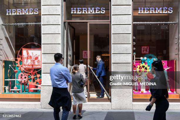People line up to enter a Hermes luxury shop on May 18, 2020 in central Milan during the country's lockdown aimed at curbing the spread of the...