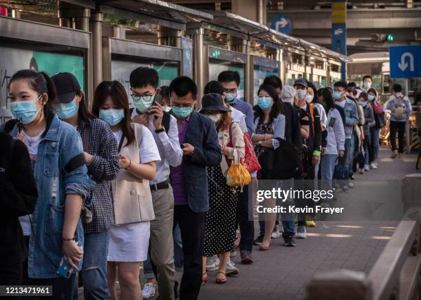 Chinese commuters wear protective masks as they line up in a crowd to catch a bus at the end of the workday during rush hour on May 18, 2020 in...