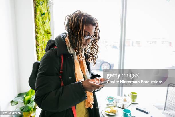 woman wearing winter coat texting on smartphone - dreadlocks stock-fotos und bilder