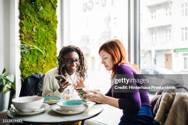 two friends looking at smartphones in cafe - purple shirt fotografías e imágenes de stock