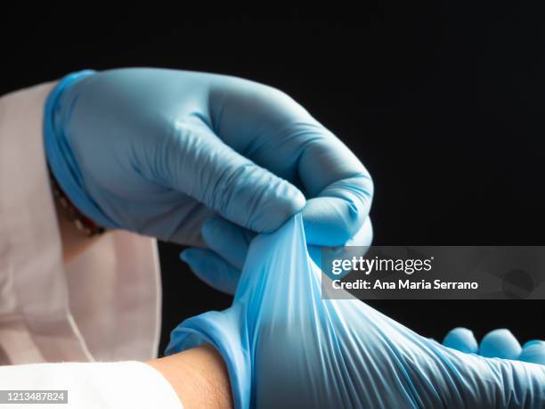 a person in a lab coat putting protective gloves on his hands - luva de borracha imagens e fotografias de stock