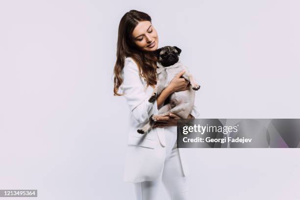 a laughing and smiling auburn haired woman in a white dress, is staring most lovingly at her cute pug, who calmly sits on the hands, gaining her undivided attention. isolated white background. - veterinary objects stock-fotos und bilder