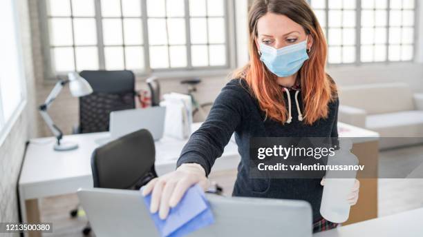 frau im büro mit desinfektionsmittel zur desinfektion der monitoroberfläche während der covid-19-pandemie - schutz und arbeitskleidung stock-fotos und bilder