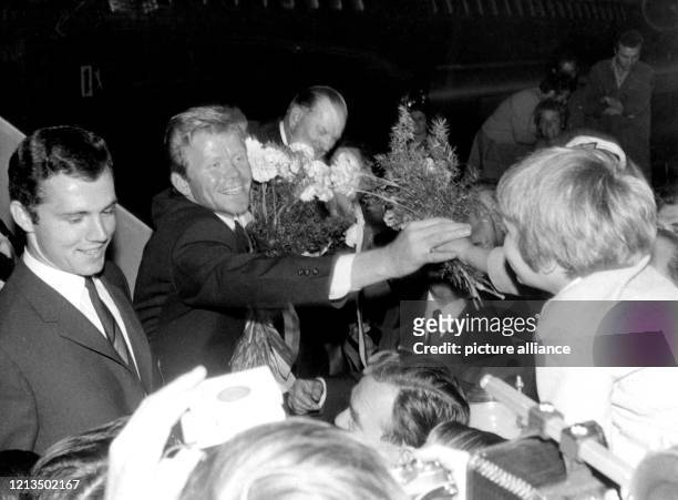 Flankiert von Libero Franz Beckenbauer , nimmt Stürmer Helmut Haller am auf dem Flughafen München-Riem lachend einen Blumenstrauß von seiner...