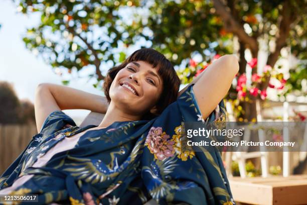 smiling woman lying back in a deck chair on her patio - deckchair stock pictures, royalty-free photos & images