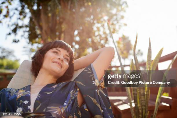 glimlachende jonge vrouw die terug in een stoel van het terrasdek ligt - tevreden stockfoto's en -beelden