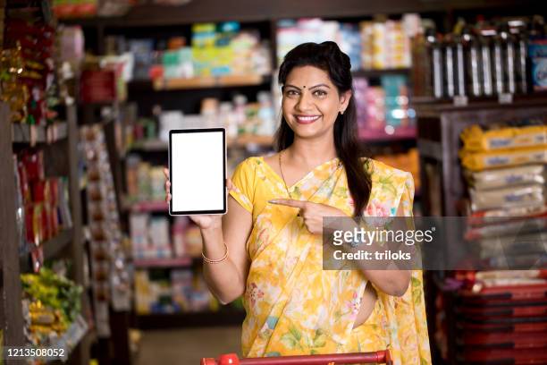 woman pointing at blank digital tablet screen in supermarket - indian shopkeeper stock pictures, royalty-free photos & images