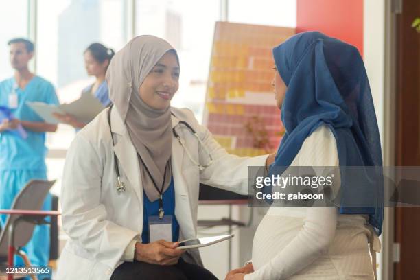muslimische ärztin im gespräch mit ihrer schwangeren patientin - indonesian ethnicity stock-fotos und bilder