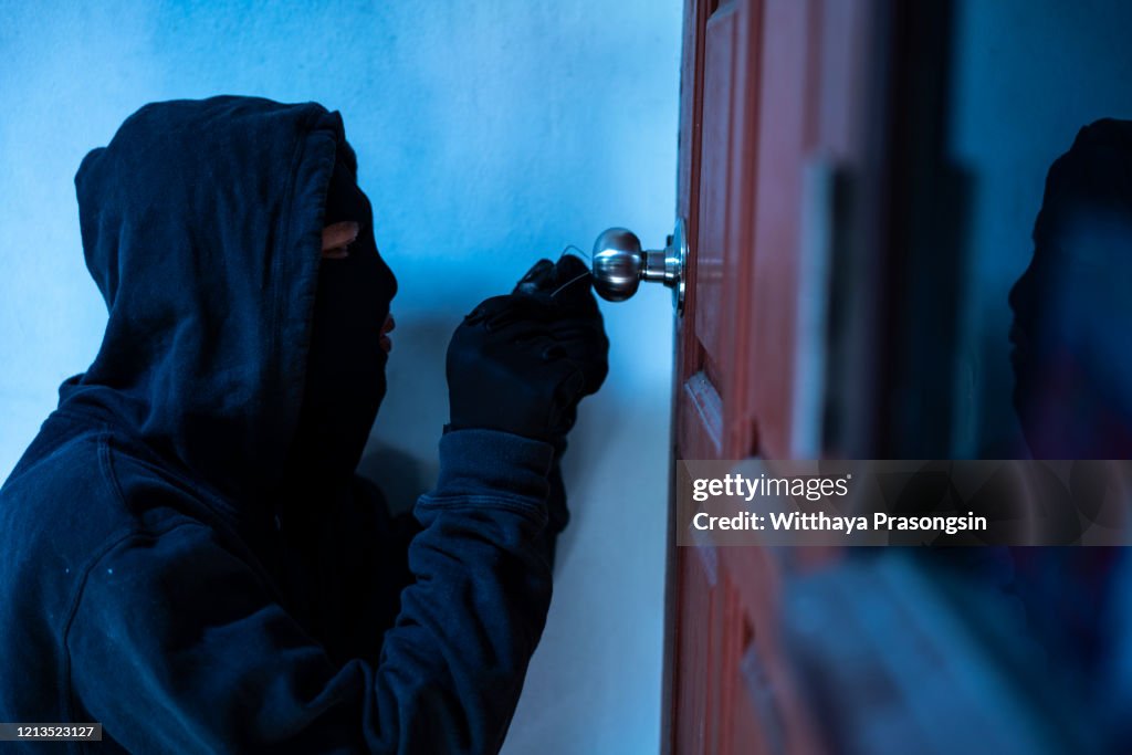 Masked thief using lock picker to open locked door