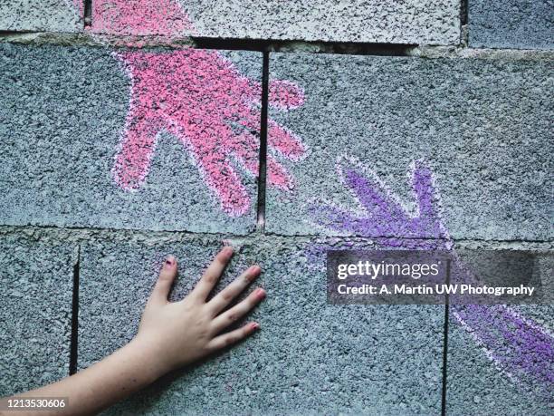 hand of a young girl touching a picture made with chalks of other hands on a concrete blocks wall. freedom and hope concept. - chalk wall stock pictures, royalty-free photos & images