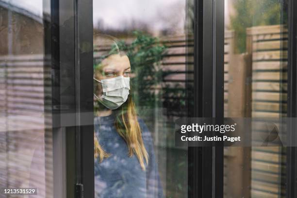 teenage girl looking through window with mask - pandemic illness stockfoto's en -beelden