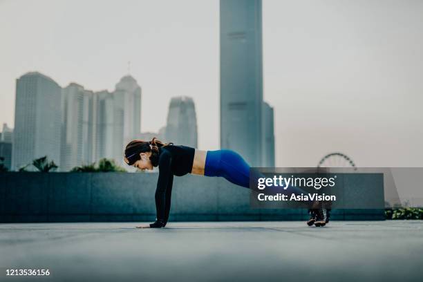 vertrouwen en energieke jonge aziatische sportenvrouw die in openlucht in stedelijk park tegen stadshorizon bij zonsondergang uitoefent en uitwerkt - woman stretching sunset stockfoto's en -beelden