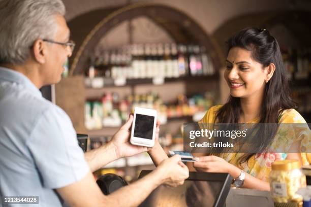 woman paying by credit card at the supermarket - indian shopkeeper stock pictures, royalty-free photos & images