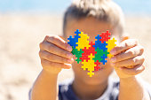 Boy holding colorful puzzle heart in front of his face. World autism awareness day concept