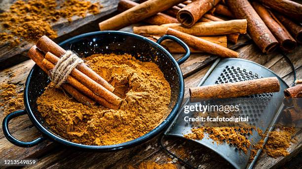 ground cinnamon and cinnamon sticks shot on rustic wooden table. - cinnamon stock pictures, royalty-free photos & images