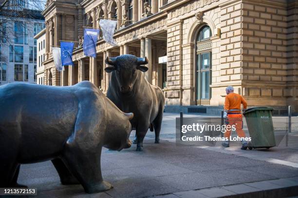Dustman carries a dustbin next to the bull statue and a bear statue outside the Frankfurt Stock Exchange on March 19, 2020 in Frankfurt, Germany....
