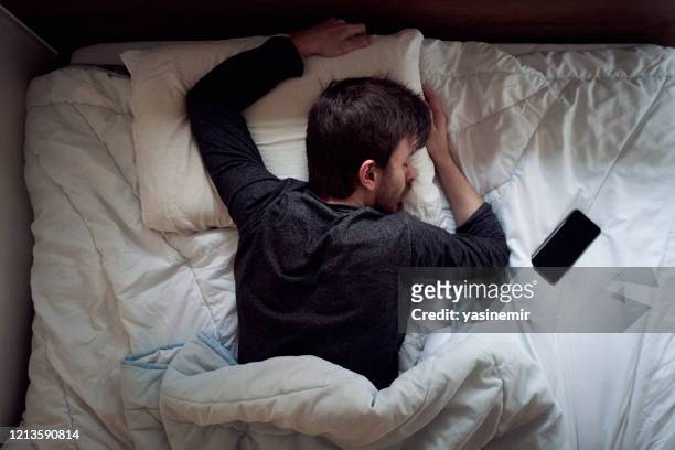 young male sleeping in the bed only himself during the day smartphone next to him - dormir imagens e fotografias de stock