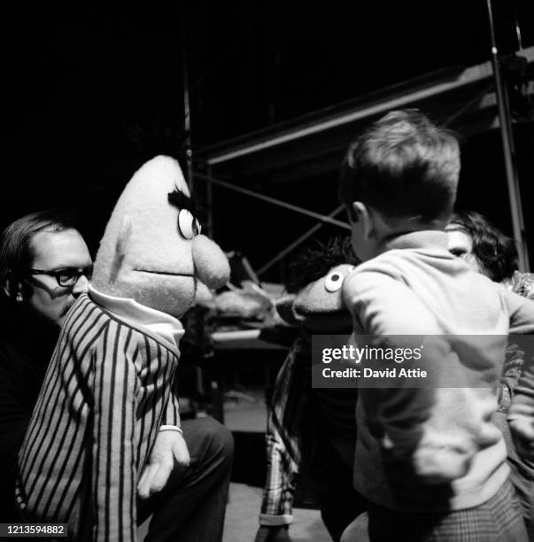 Puppeteers Frank Oz holding Bert and Jim Henson holding Ernie entertain a child during rehearsals for an episode of Sesame Street at Reeves TeleTape...